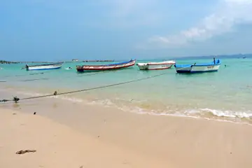 নিল দ্বীপের ফ্যাকাশে বালির সৈকতের কাছে ফিরোজা রঙের অগভীর জলে বাঁধা রং করা কাঠের মাছধরা নৌকো