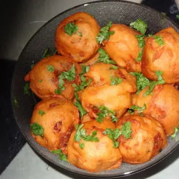 A dark bowl of fried potato bonda sprinkled with chopped coriander