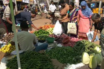 Shoppers with cloth bags at a vegetable seller's heaps of okra, chillies, tomatoes and gourds in Kakinada