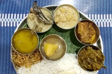 A steel thali with white rice, dal and several curries in small bowls on a banana leaf