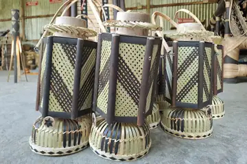 Tall woven bamboo lanterns with dark frames standing on round woven bases in a workshop