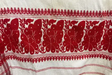 A white gamosa with a broad red woven border of flowers and thin red stripes