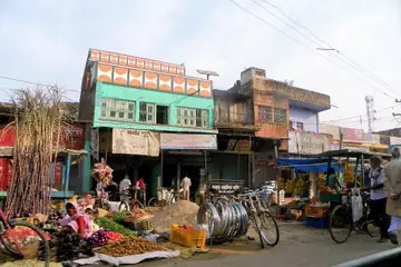 A roadside market corner in Bihar with sugarcane stalks, vegetables on mats and a green and orange shop front