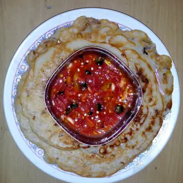 A golden dhuska fried rice-flour round with a bowl of roasted tomato chutney in the middle