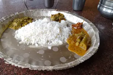 A foil plate of rice with dal, a drumstick curry and a green side dish, in Konta, Chhattisgarh
