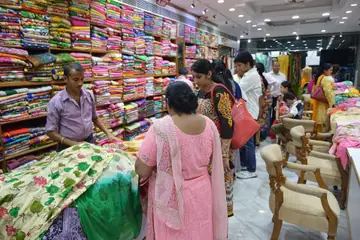 A cloth shop at Bridge Market in Chandigarh with shelves of folded fabric and customers being shown suit lengths