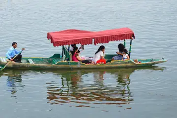 A red-canopied shikara boat on Sukhna Lake in Chandigarh with a boatman and a family