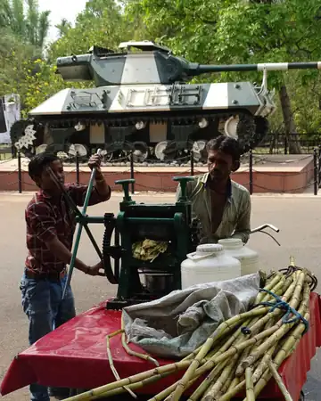 Two men pressing sugarcane juice at a cart with a bundle of cane beside it.