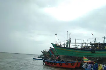 Green and red fishing boats with black tyre fenders tied up side by side at a port in Diu