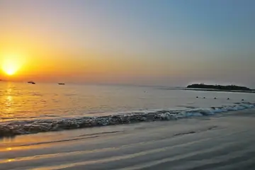 દીવમાં દરિયાકિનારે ધીમાં મોજાં પર ઊગતો સૂરજ, ક્ષિતિજ પર નીચો ટાપુ