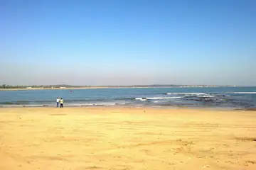 A wide beach of pale yellow sand under a bright blue sky at Nagoa Beach in Diu, the sea beyond and two people far off