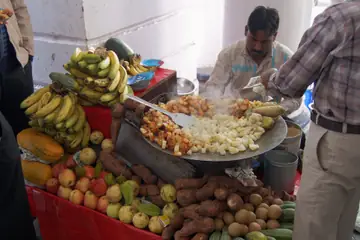 कनॉट प्लेस में केलों और शकरकंद के पास सपाट तवे पर आलू चाट हिलाता एक बेचने वाला
