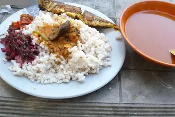 A plate of boiled rice with fish curry and a red side dish, and a bowl of red curry beside it, at Rachol, Goa
