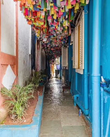 A narrow lane between blue and white houses in Panaji, with rows of coloured paper flags strung overhead