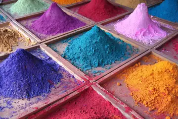 Heaps of pink, blue, violet, orange and red powder pigments in square trays at a market stall in Goa