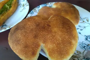 A round, golden-brown bread, torn open, on a flowered plate