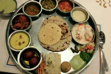 A round steel thali with small bowls of dal, vegetables, kadhi and sweets, a roti and a papad