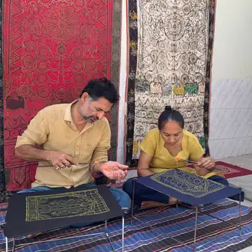 Dhaaridaar dari par baithe ek aadmi aur ek aurat kaale kapde par rogan kala bana rahe hain