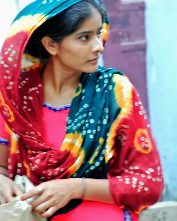 A young woman in a bright red, blue and green bandhej shawl, looking to the side