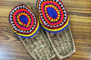A pair of woven Himachali paule slippers with bright round patterns in red, yellow, blue and white wool on a wooden table