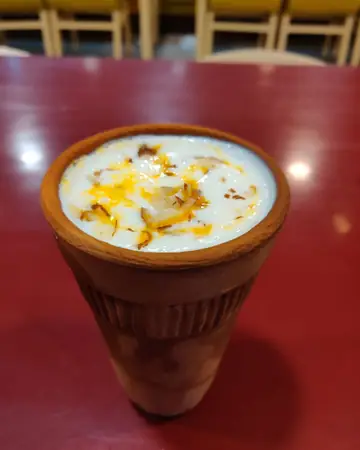 Thick lassi in a clay cup, topped with cream and saffron