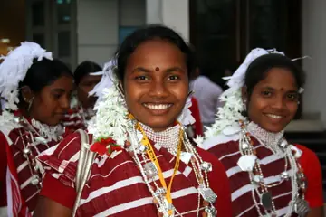 Laal dhaariyon wale kapde, safed phoolon ki maala aur chaandi ke haar mein do muskurati Kharia mahilayen