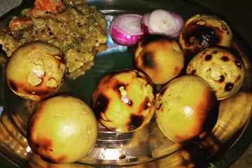 Roasted litti balls with chokha and sliced onion on a steel plate