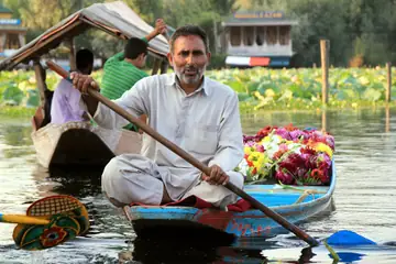 A boatman on a shikara with a heap of fresh flowers to sell.