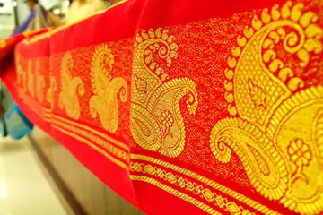A red silk saree border with golden paisley woven into it