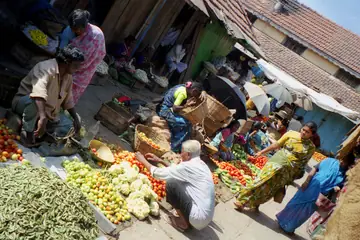 Sellers and buyers around heaps of tomatoes, cauliflower and beans on the ground at Devaraja Market, Mysuru