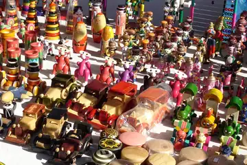 Colourful wooden toy cars, dolls and tops laid out on a stall in the sun