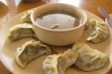A plate of steamed momos with a bowl of clear broth in a Leh restaurant
