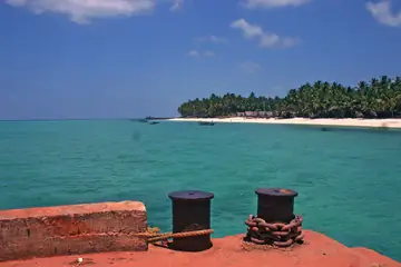 Two iron mooring bollards on a red stone jetty at Agatti, with the lagoon and a palm-lined shore beyond