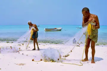 Two fishermen untangling and mending a fishing net on the white sand beach at Kavaratti