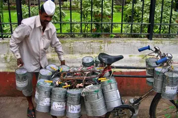 A man in a white cap beside a bicycle loaded with steel lunch tins in Mumbai