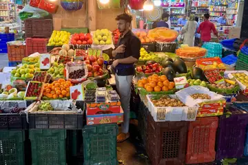 Mumbai ke Crawford Market mein roshni se jagmagate stall par santre, seb, angoor aur anaar ki peti ke beech khada phal wala