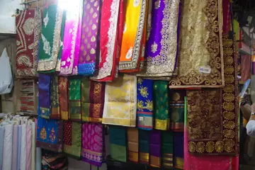 Mumbai ke Crawford Market ki kapde ki dukaan mein tange hue hare, gulabi, peele aur baingani rang ke saadi aur kadhai wale kapde
