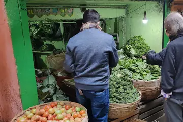 Two customers choosing greens and tomatoes from baskets at a small vegetable shop in Shillong