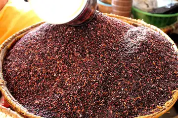 Dark black glutinous rice heaped in a cane basket, being poured from a scoop