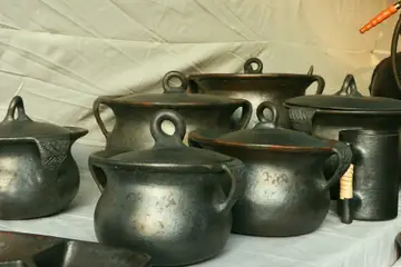 A group of black clay cooking pots with lids and loop handles, on a cloth-covered table