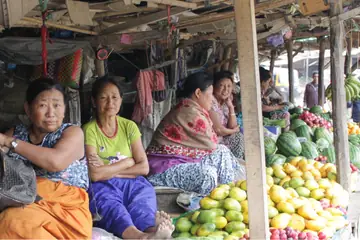Three women sitting at their fruit stall in Senapati, with papayas, melons and bananas heaped beside them