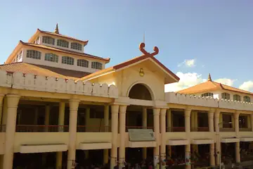 A two-storey market building with pillars, an arched entrance and pagoda-style roofs, with people under its arcade in Imphal