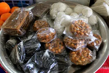 A steel tray of wrapped puffed-rice, sesame and groundnut sweets with oranges beside it in Imphal