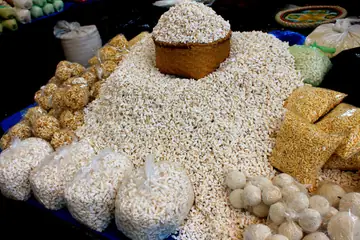 A heap of puffed rice with a basket on top, and bags of puffed-rice sweets around it at Ima Keithel in Imphal