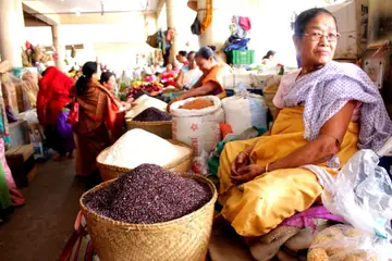 A woman in a yellow wrap sitting by baskets of black and white glutinous rice at Ima Keithel in Imphal