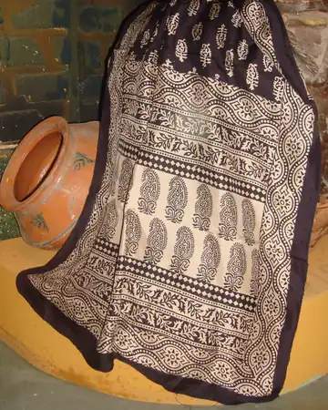A black and cream Bagh block-printed stole with paisley rows hung beside a clay pot