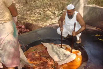 A man in a white vest stirring printed cloth in a large vat of dye water over a fire