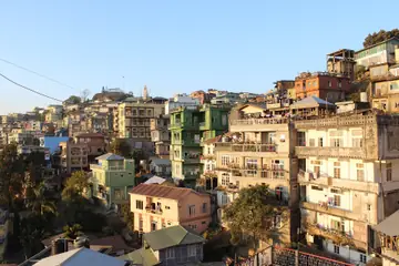 Tall houses and shops stacked up a hillside in Aizawl in morning light