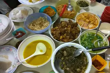A table laid with bowls of curries, greens and pickles and a stack of plates