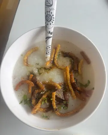 A white bowl of rice porridge topped with fried strips, with a spoon in it